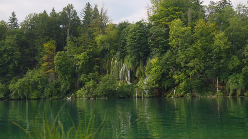 Calm emerald lake reflecting forest and waterfalls at Plitvice Lakes National Park, Croatia.