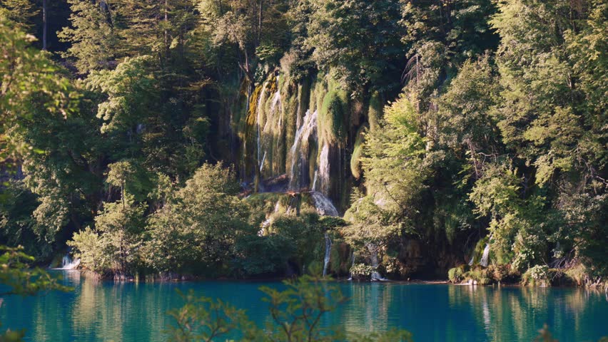 Lush forest waterfalls flowing into a turquoise lake at Plitvice Lakes National Park, Croatia.