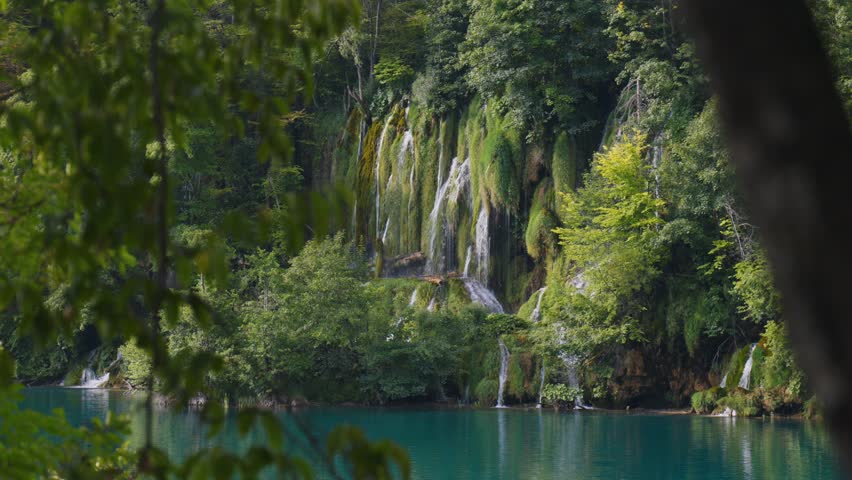 Waterfalls and turquoise lake framed by forest branches at Plitvice Lakes National Park, Croatia.