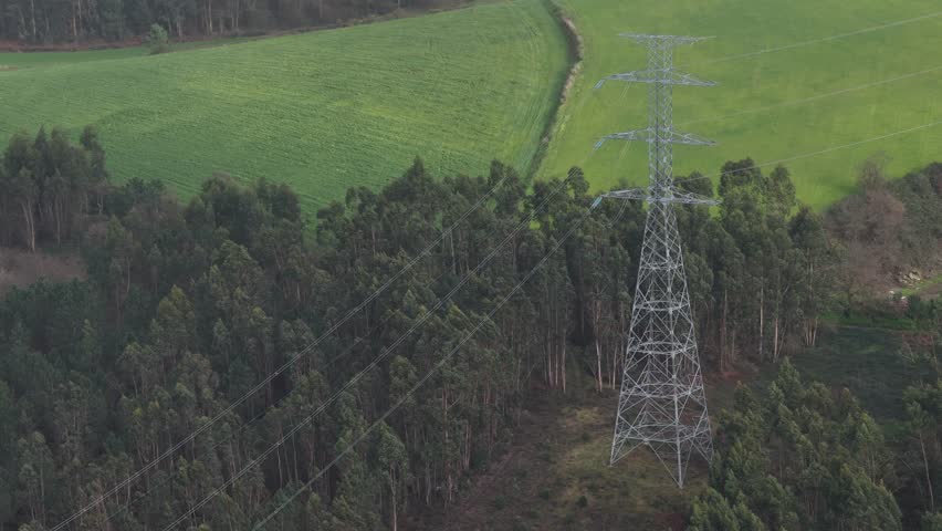 Tall power transmission towers and lines in the middle of the forest and farming fields