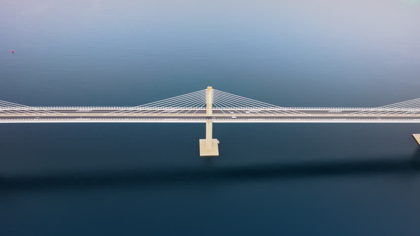 Aerial drone view of the Peljesac Bridge near Komarna, Croatia, partially shrouded in low coastal fog with mountains in the background