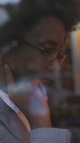 Focused young african woman in business suit drinking coffee during break while sitting at cafe table. Concept of remote work, people and technology.