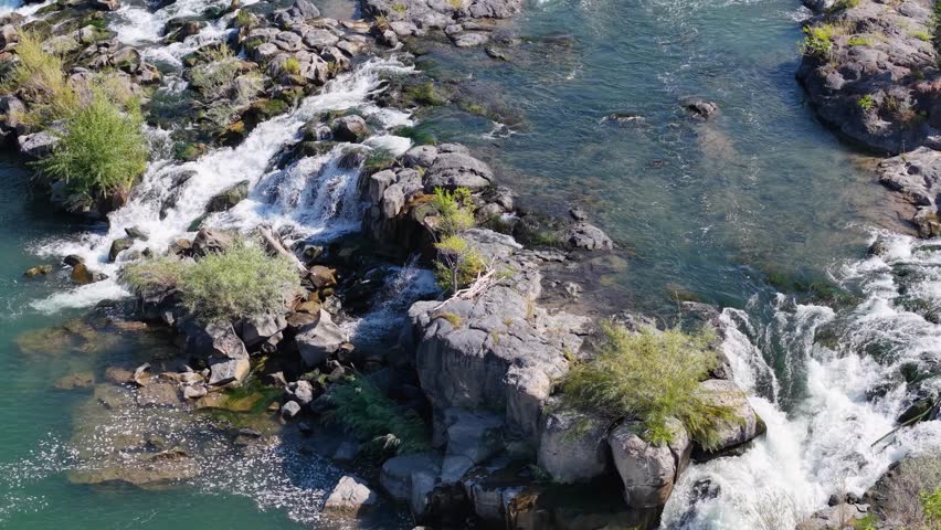 A drone shot of a river cascading over rocky islands with lush vegetation, showing whitewater swirling around the rocks Idaho Falls