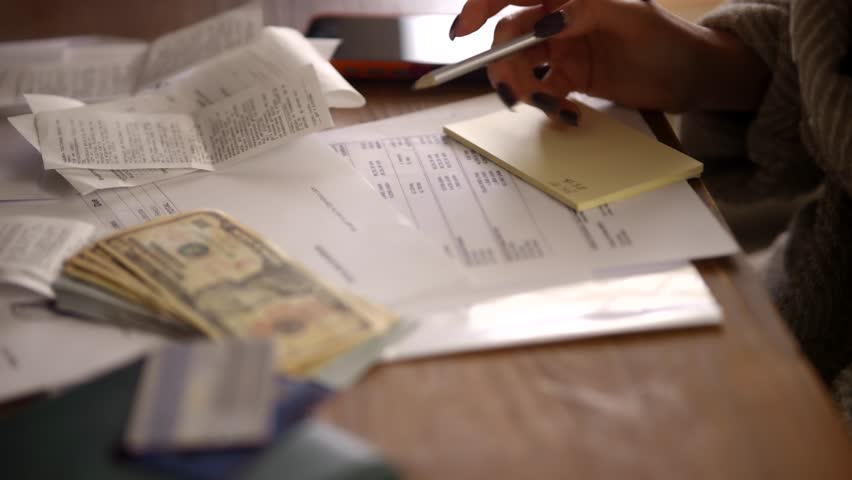 Payer Writing Notes Near Paper Receipts To Calculate Utility Debt At Home, Financial Management Process With Payer Reviewing Paper Receipts And Invoices, Economy Budget Planning, Homeowner Analyzing Utility Debt Using Smartphone Near Cash, Household Expenses Documentation, Payment Records For Utility Debt And Paper Receipts