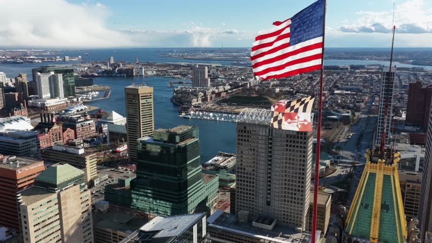 Waving flag of America and Maryland on top of WILLIAM DONALD SCHAEFER TOWER in downtown of Baltimore. Sunny day with blue sky in USA. Aerial close up shot.