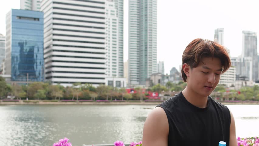 Medium shot of a sporty man drinking water from a plastic bottle in a park
