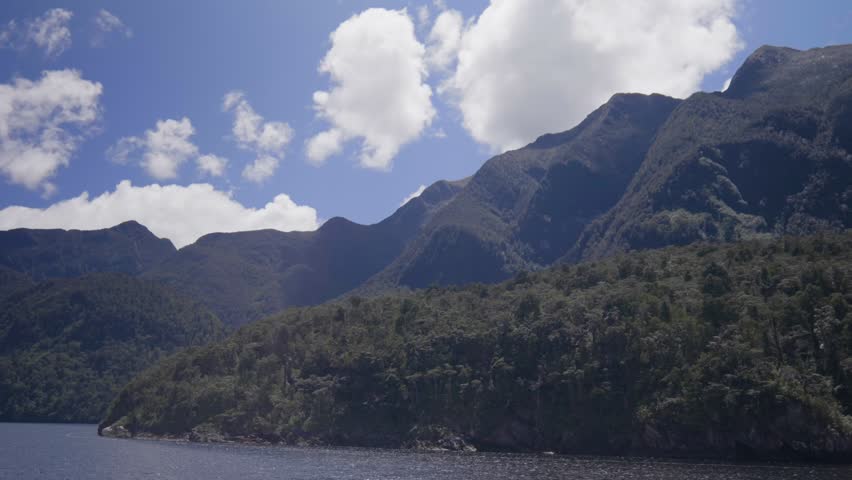 Towering mountains rise above Doubtful Sound, showcasing dramatic peaks, deep fjords, and pristine wilderness in a remote, cinematic New Zealand landscape.