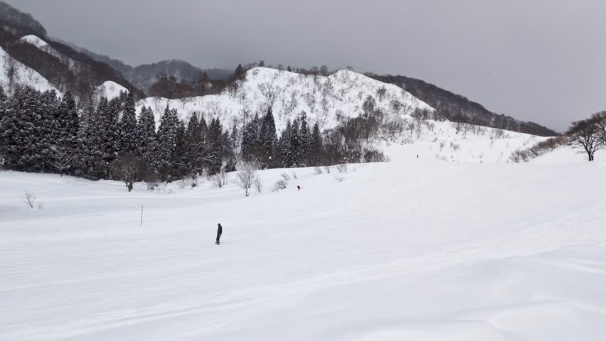 Winter scene of person snowboarding down wide run in Japanese Alps, Nagano