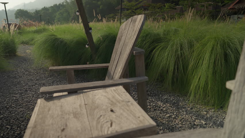Morning atmosphere of a cozy glamping spot with a wooden tipi structure, table, and chairs in a lush green meadow with white wildflowers.