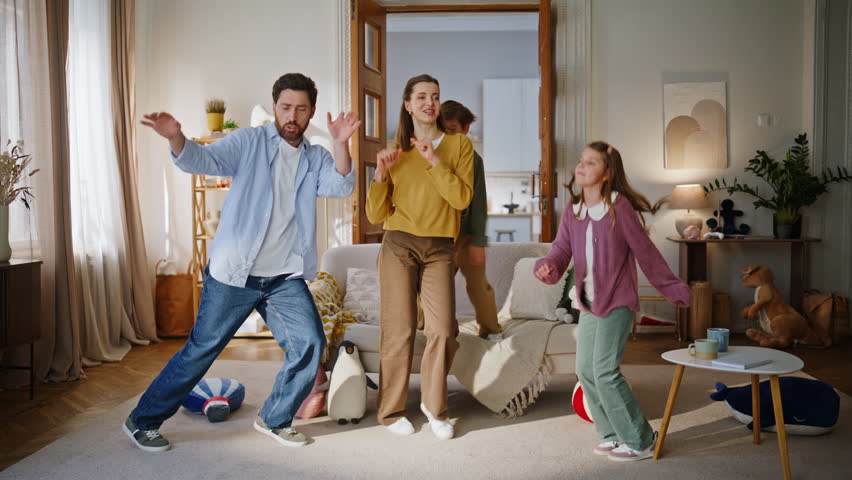 Carefree family jumping home having fun together. Positive people relatives dancing celebrating party laughing light cozy apartment. Little boy girl with parents listening music. Happiness concept