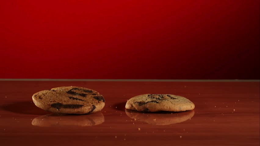 Delicious round chocolate chip cookies falling and stacking on a polished wooden surface against a vibrant red background in a professional slow motion studio