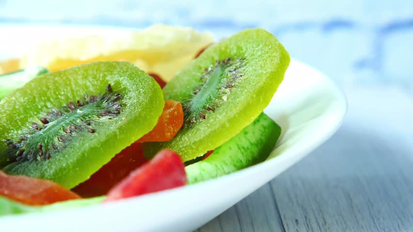 This video documents slices of dried and candied kiwi fruit. The visual captures the preserved green flesh and the characteristic radial seed pattern of the Actinidia deliciosa. The composition illustrates the translucent texture resulting from the preservation process, representing dried fruit snacks, food preservation techniques, and trail mix ingredients in a high-resolution format.