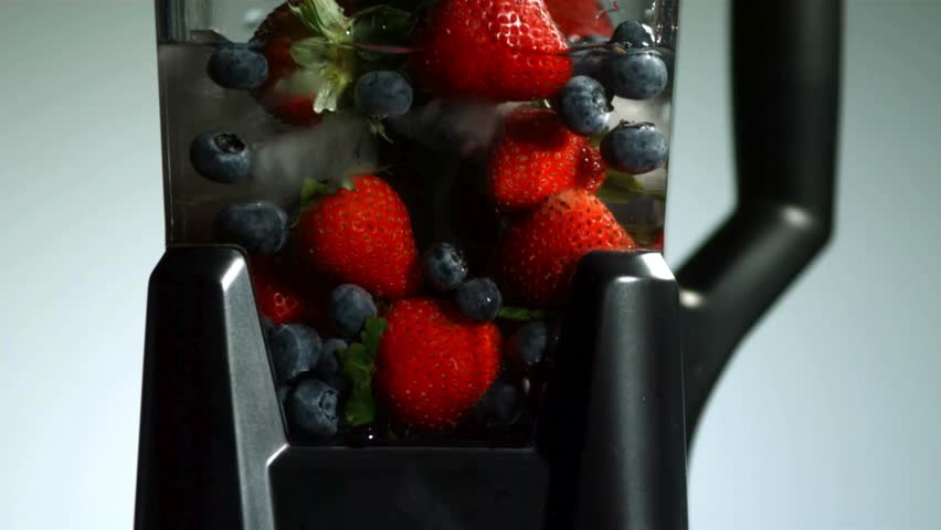 Fresh strawberries and blueberries with ice cubes being mixed and swirled inside a black electric blender to make a healthy fruit smoothie in a studio kitchen setting