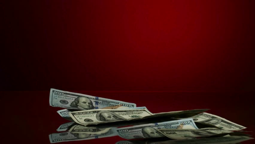 United States one hundred dollar bills falling onto a large pile of cash money spread across a dark red reflective surface in studio