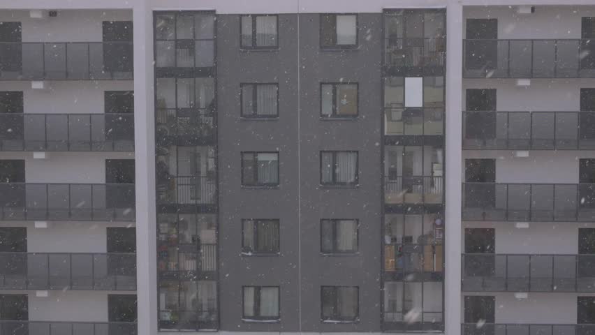 View of a residential building from an apartment window with balconies, as snowflakes fall continuously in a winter setting. Winter view from a window