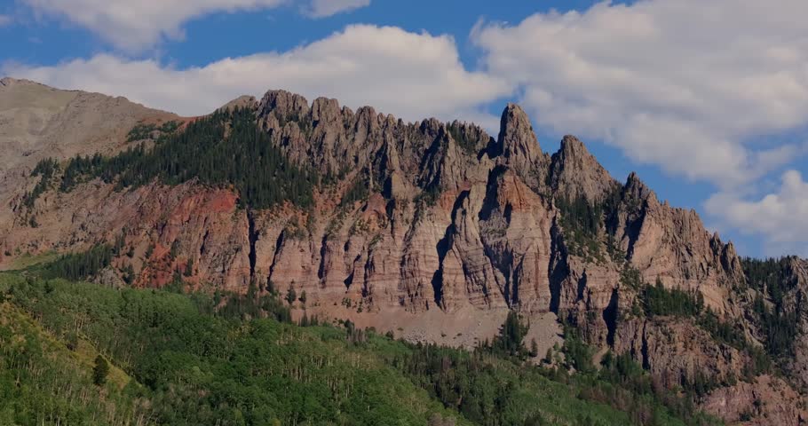 Jagged red rock cliffs rise above green forest in dramatic mountain landscape, Highway 145 Colorado USA