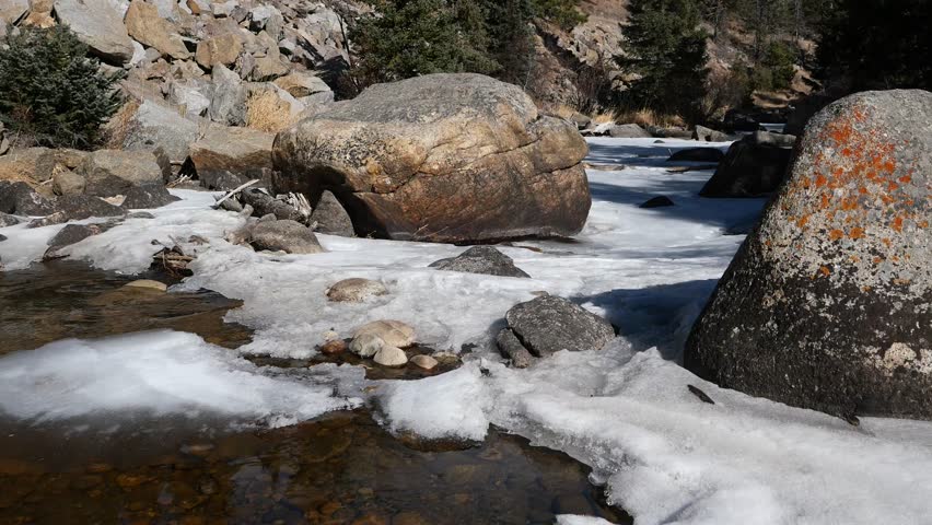 4K partially frozen mountain creek flowing through rocky canyon in winter, Colorado