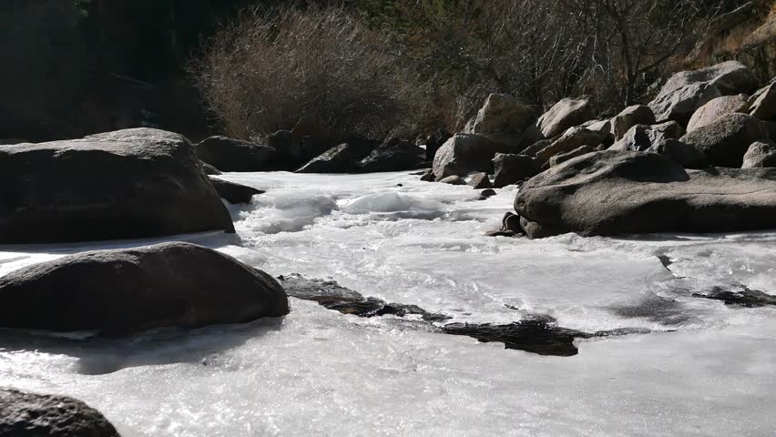 4K partially frozen mountain creek with flowing water under ice in winter, Colorado