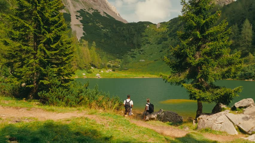 Two hikers enjoy serene lake views in Dolomites, Italy, surrounded by nature