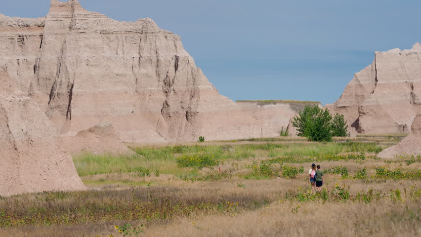 Travelers walking along trails in Badlands National Park, passing layered cliffs and open prairie, outdoor adventure, scenic geology, summer exploration of iconic desert wilderness, active vacation and travel discovery