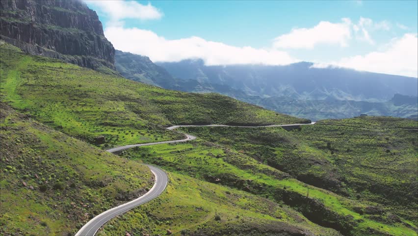 Panoramic mountain landscape in Gran Canaria, Tasarte, along Ruta Ciclista near Inagua peak and Los Azulejos de Veneguera, with winding roads, green valleys and dramatic cliffs under blue sky.