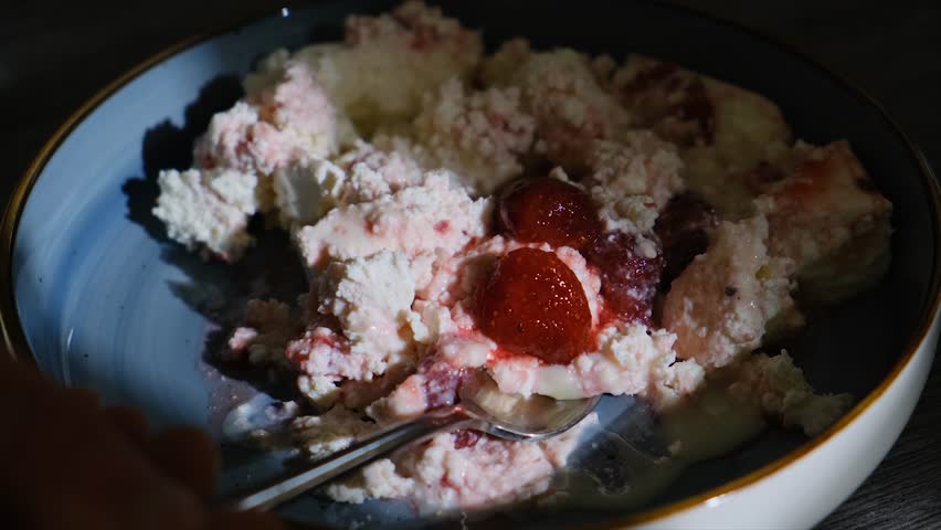 Spoon takes milk cottage cheese with sweet strawberry jam and whole strawberry. Berries mixed with low fat cottage cheese in a dessert, diet breakfast concept.
