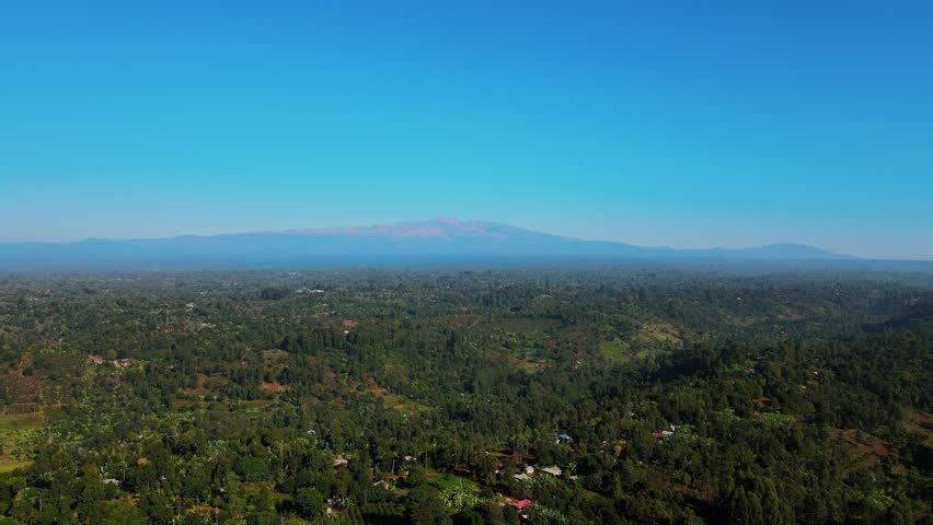 Breathtaking aerial shot of the Mount Kenya peaks on the horizon overlooking the dense tropical forests and rural landscape of Embu County. Ideal for travel documentaries and nature conservation conte