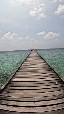 Walking along the pier with a beautiful azure sea on a local Maldivian island, vertical