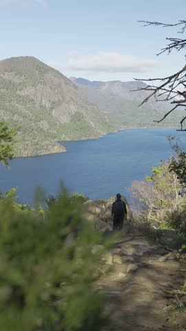 Man stands on a rock overlooking a lake, capturing photographs in a peaceful natural setting.
