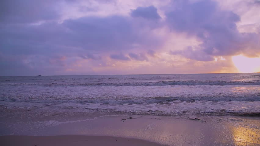 Slow motion view of a pink sunset at the beach. Footage showing calm sea, sandy coastline, and warm pink light during sunset. 