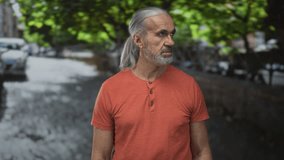 Man with gray beard and long hair looking up on tree lined street in orange shirt and gold chain; serenity reflection. - Powered by Shutterstock - Get 15% off with code: PIKWIZARD15