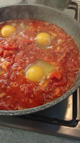 Shakshuka steaming in pan with eggs cooked in tomato sauce on stove. Concept of hot homemade meal, traditional cuisine and comfort food