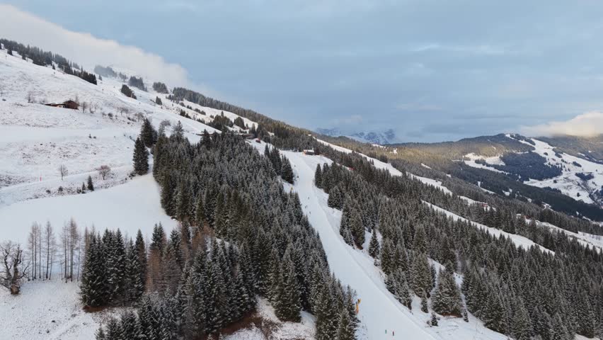 Aerial view of ski resort in the Alps with skiers on a snowy slope surrounded by a forest during winter holidays in Austria