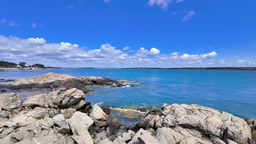 Slow motion view of Cape Forchu Nova Scotia coastline with ocean waves hitting rocky shore under clear blue sky in bright summer daylight creating a scenic Atlantic coastal landscape