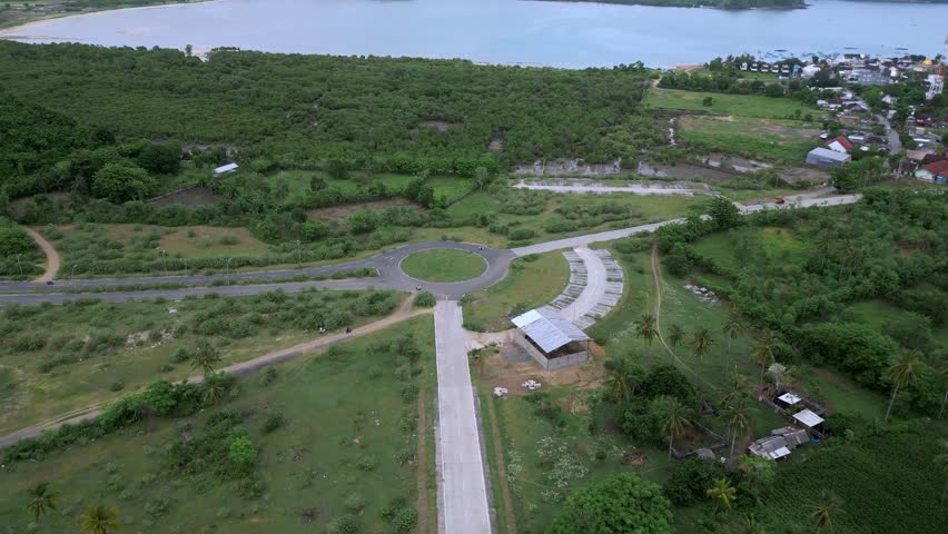 Aerial Coastal Crossroads Winding Road Village. Lush Hillside, Roundabout, Distant Coastline, Scattered Houses And Empty Fields. Scenes Include Farmer Tending Crops,Gerupuk,Lombok,Indonesia