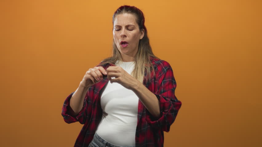 Woman stretching a yellow tape measure with hands, mouth open in surprise while wearing a red plaid shirt in studio; surprise measurement.