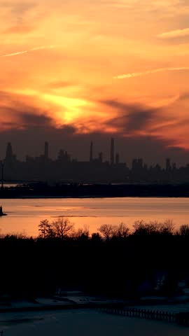Beautiful golden hour sunset casting a warm glow over the water, with the iconic silhouette of the new york city skyline standing out against the vibrant, cloudy sky during a winter evening