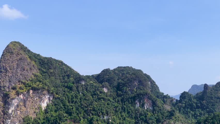 A slow horizontal pan across lush green limestone mountains under a clear blue sky