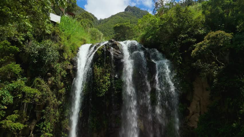Aerial rising above the elegant Cascada El Silencio waterfall flowing down a mossy cliffside surrounded by dense tropical rainforest near Banos de Agua Santa, Ecuador