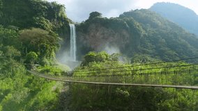 Drone shot rising to reveal Manto de la Novia waterfall plunging into lush valley with hanging pedestrian bridge over river in Baños Ecuador mountains - Powered by Shutterstock - Get 15% off with code: PIKWIZARD15