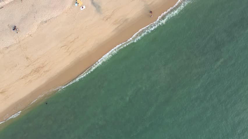 A high-angle aerial view of a clean sandy beach in Penang, showing tourists relaxing under umbrellas and a lone blue kayak resting near the turquoise shoreline.