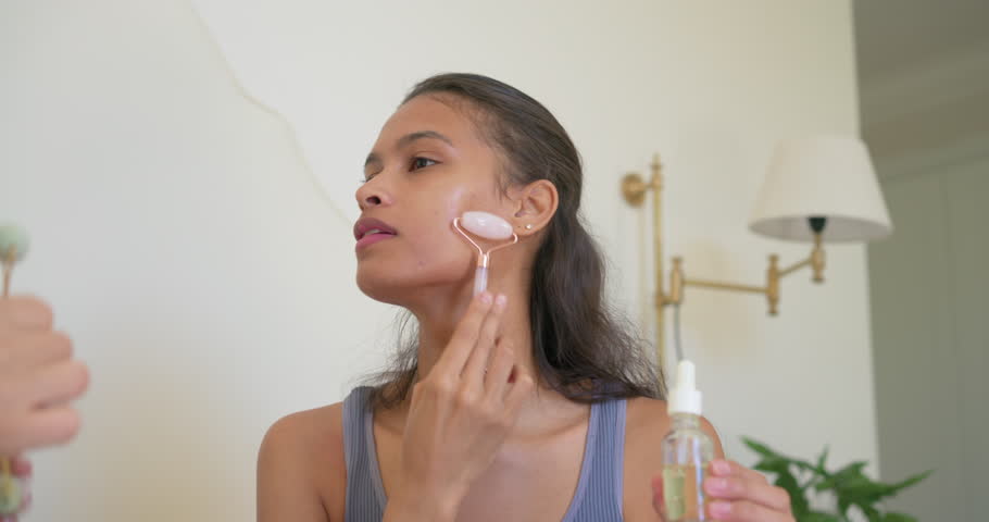 Diverse female friends sharing skincare at vanity, dispensing oil and rolling pink and green stones. Jade, roller, serum, duo, women, lifestyle, ambient