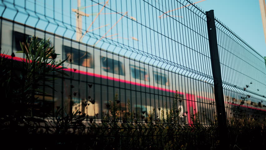 Blurred motion of a modern train seen through a wire fence with blue sky background