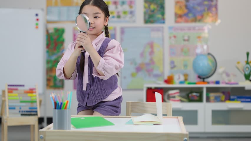 Young girl with braids investigates objects using magnifying glass at brightly lit classroom desk