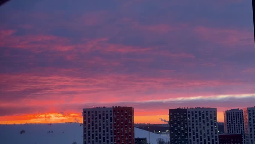 Vibrant sunset sky with pink and orange clouds over modern residential apartment buildings. Urban skyline at dusk with sun glowing on the horizon. Cityscape and real estate concept.