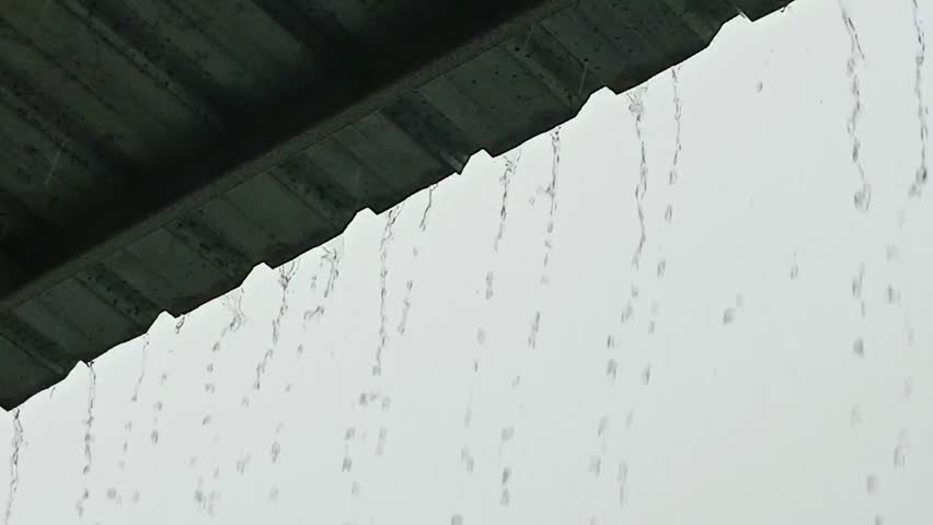 Heavy rain falling from a corrugated metal canopy roof against a grey sky.