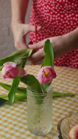 Vertical video. Spring season, mother's day or women's Day. Woman clipping tulips flowers and putting them in a vase in kitchen
