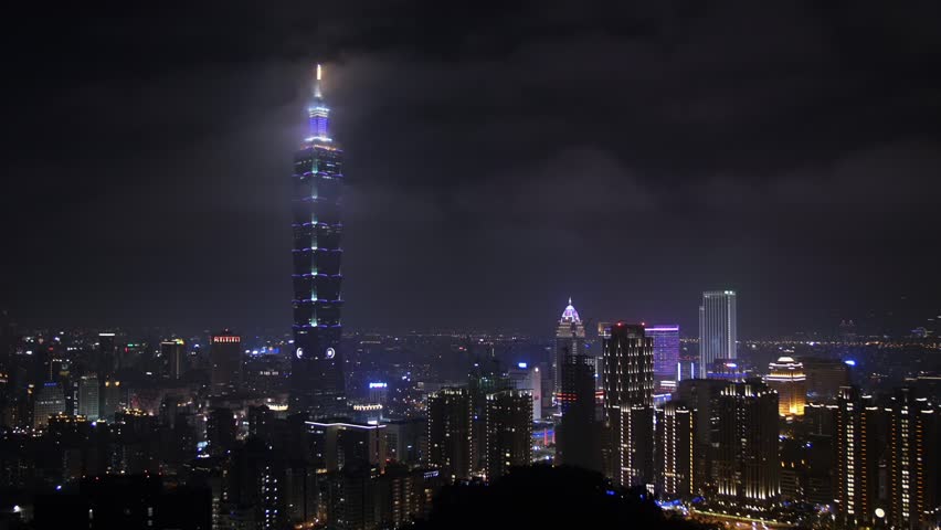 Nighttime city skyline of Taipei, Taiwan, with illuminated skyscrapers and vibrant urban lights reflecting on the city.