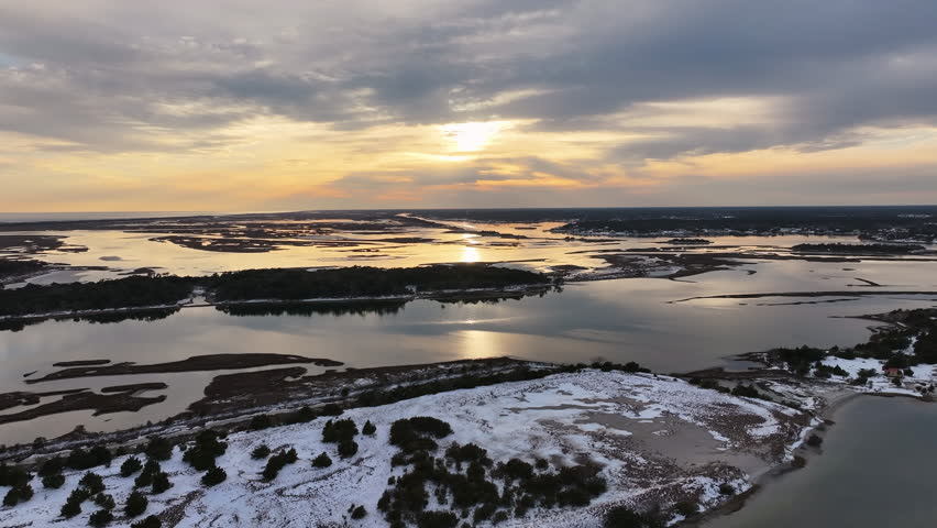 Aerial view of the Crystal Coast barrier islands, where rare snowfall blankets sandy shorelines and ice forms across the coastal marshes. drone footage.