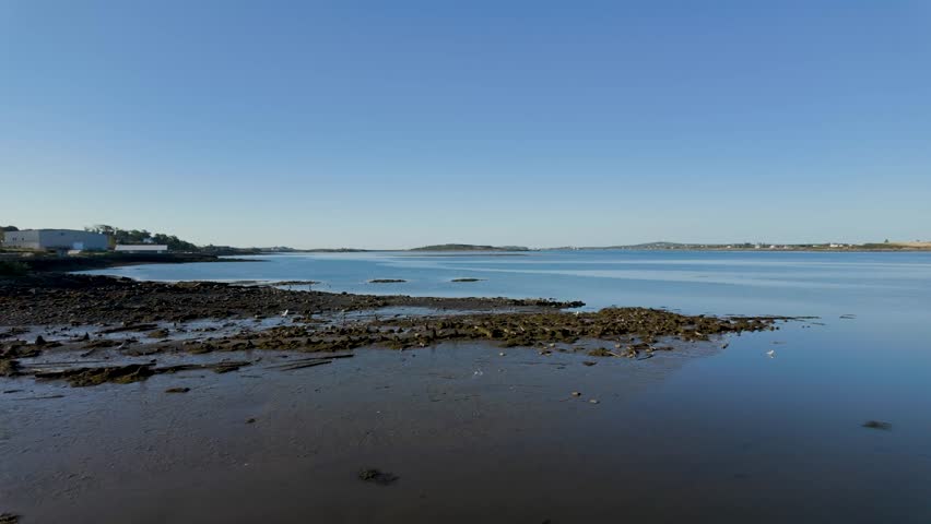 Scenic coastal landscape overlooking Yarmouth Harbour in Nova Scotia Canada featuring exposed rocky shoreline at low tide calm Atlantic waters and distant waterfront beneath a clear blue sky showcasing the natural beauty of Canada’s eastern coast